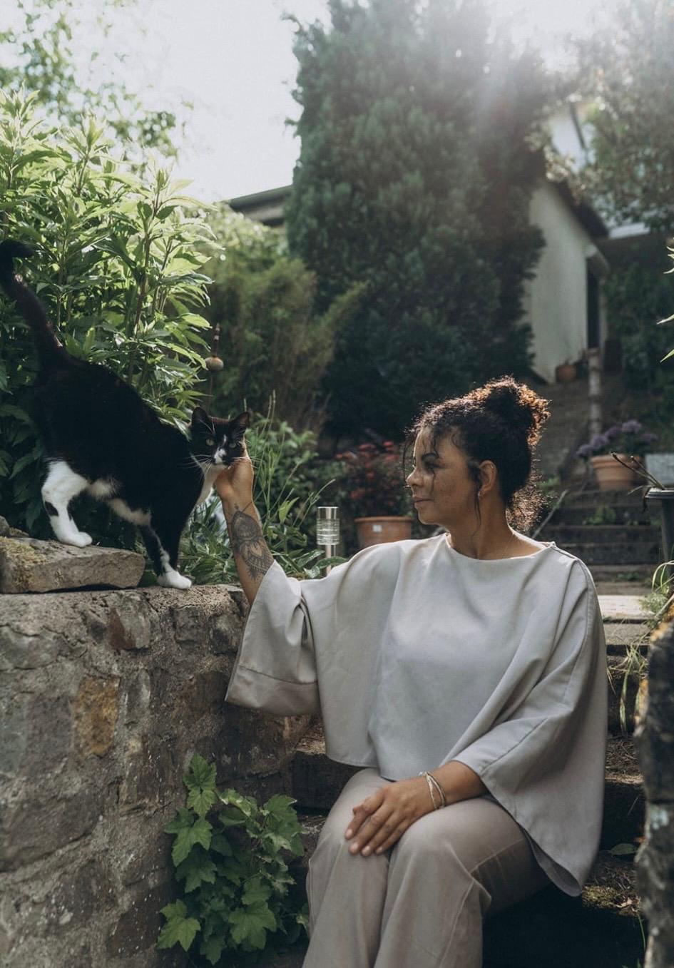 Stefanie reicht im Garten einer Katze die Hand, warmes Tageslicht