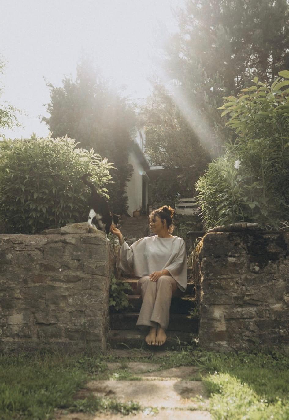 Stefanie sitzt auf alten Steinstufen im Garten, Sonnenlicht fällt durch die Bäume